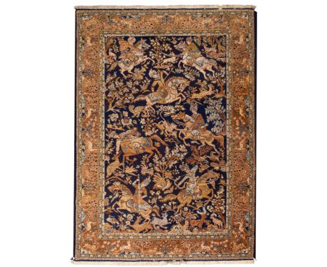 A Kashmiri rug, the indigo field with equestrian hunting figures and trees and flowers, enclosed by a main light brown border