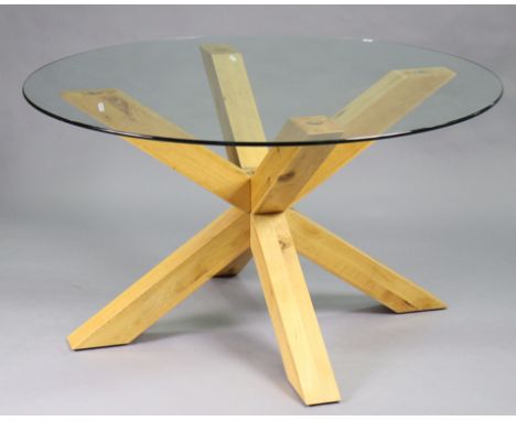 A modern dining table with circular tempered glass top, on a light-oak shaped pedestal base, 55” diameter x 30” high.