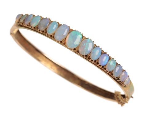 A VICTORIAN OPAL BANGLE the graduated blue tone opals half-set on a unmarked rose-coloured metal hinged bangle, with attached