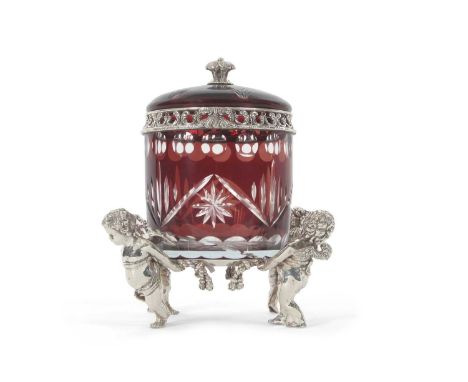 A figural putti silver plated bon bonniere, the flash cut ruby glass barrel with pull off domed cover with a decorative bud f
