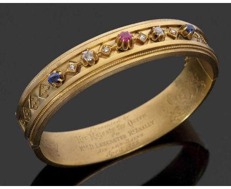 A Queen Victoria presentation bangle, the hinged bangle, 13mm wide, set to centre with a claw mounted ruby, with a round and 