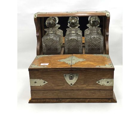 An Edwardian oak three decanter tantalus, having a hinged cover opening to reveal a fitted interior, with draw below, w.36cmA