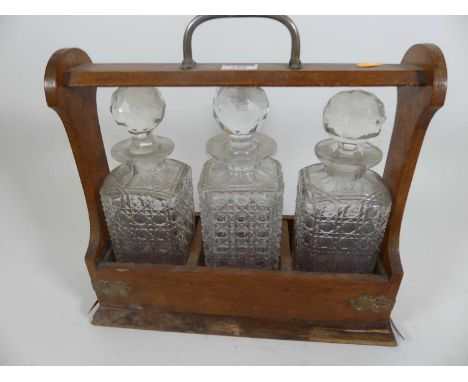 An Edwardian oak three decanter tantalus, width 34cm (a/f)The three decanters are different sizes, the largest h.22.5cm, w.8c