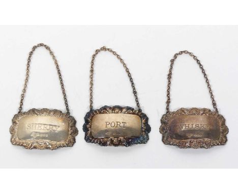 A matched set of three Elizabeth II silver decanter labels, each having a shell and foliate repousse decorated border, engrav