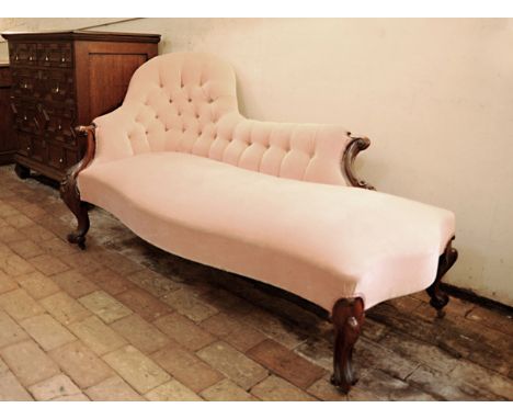 A Victorian chaise longue with puce upholstered button back, stylised flower head and acanthus leaf carved scrolled arm termi