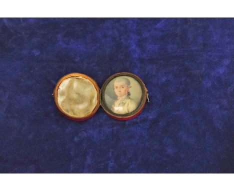 An oval portrait miniature of a gentleman wearing a powdered wig and lace cravat, in a red leather folding frame. 