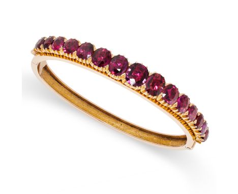 AN ANTIQUE UNHEATED RUBY BANGLE in yellow gold, set with a single row of graduated cushion cut rubies all totalling 11.00 car