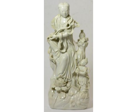 A Chinese Blanc de Chine Figure of Guanyin, Qing Dynasty, sitting on a rocky outcrop, an attendant at her feet, on a scroll m