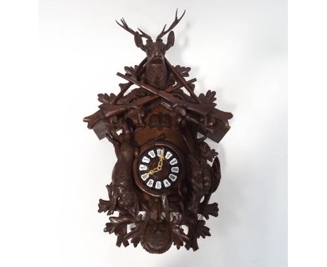 A Black Forest triple weight cuckoo clock with carved Stag head crest above two crossed guns, the dial with applied enamel nu