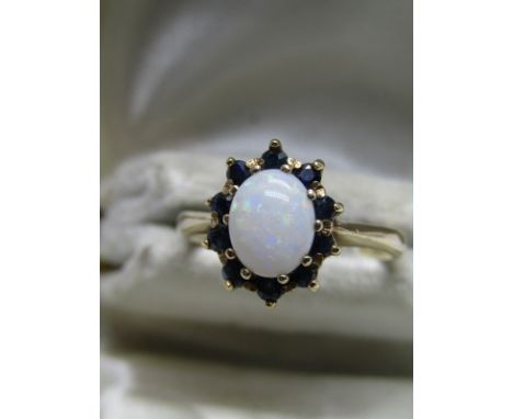 9ct YELLOW GOLD OPAL &amp; SAPPHIRE CLUSTER RING; Central oval cut opal surrounded by 10 brilliant cut blue sapphires in heav