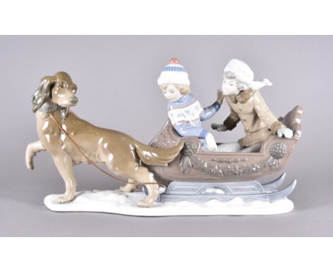 A boxed Lladro figure, modelled as children in dog drawn sleigh on modern plinth, 25 cm high x 25 cm long (without plinth)Sig