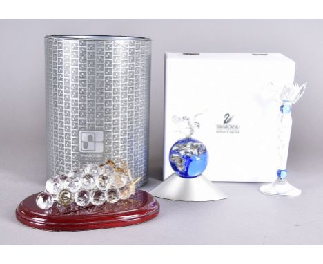 A collection of Swarovski crystal, comprising a bunch of grapes with wooden stand, a candlestick, and a crystal planet surmou