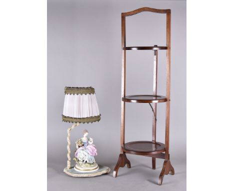 A mahogany three tier folding cake stand, together with a Capo di Monte figural table lamp surmounted with lady seated with b