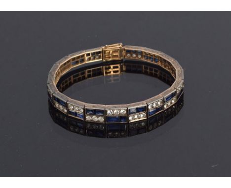An Art Deco sapphire and white topaz panel bracelet, the 49 sapphires being baguette and princess cut, mounted in silver with