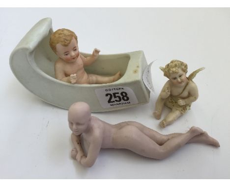 Three various early 20th century Bisque china figures modelled as a Nude Female, Cherub and Baby in a Cot.