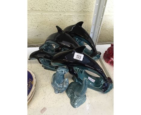 Four various Poole Pottery dolphins together with a blue glazed Otter and Seal.