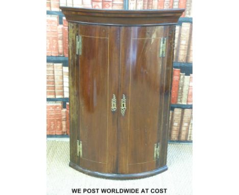 A Georgian bow fronted mahogany corner cupboard with brass hinges (H107 x W75 x D51cm)