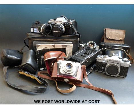 A collection of cameras including an Olympus CM10 with spare lens, Praktica PLC3 and large Kodak folding camera