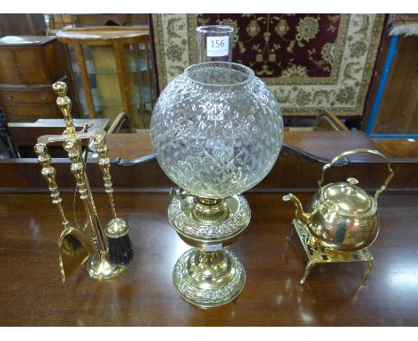 A brass oil lamp with glass shade; a brass kettle and trivet and a brass companion set