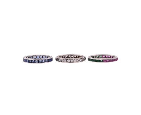 
	
		A TRIO OF ETERNITY RINGS
		The first set with step cut emeralds to one side and rubies to the other, in a silver coloure