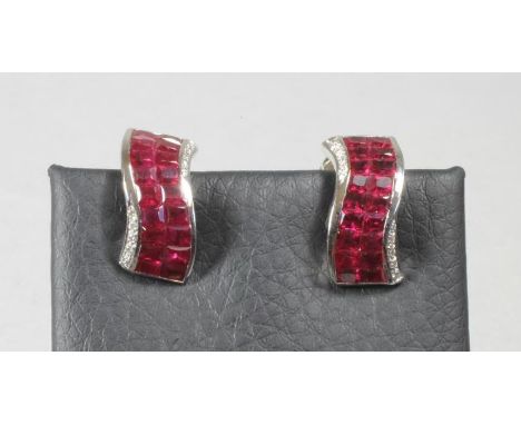 A PAIR OF RUBY AND DIAMOND EAR STUDS, each scroll plaque pave set with eighteen calibre cut rubies with five small diamonds t