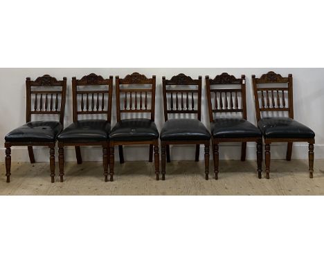 A set of six late Victorian floral carved walnut dining chairs with black leather upholstered seats and raised on ring turned