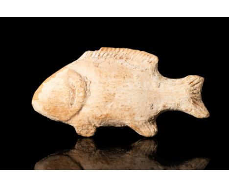 Ca. 400 BC. A pale stone amulet in the form of a fish, with a broad, ovoid body and a narrow tail ending in a notched caudal 