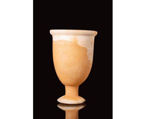 Ca. 1938 - 1190 BC. An Egyptian alabaster conical cup with an enlarged rim. The cup sits on a flat round tall pedestal base. 