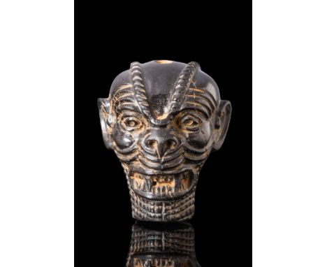Ca. 800 - 600 BC. A black stone amulet in the form of the head of the demon god Pazuzu, depicted with exaggerated facial feat
