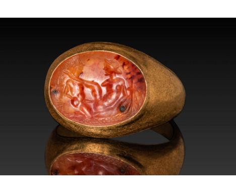 Ca. AD 1 - 200. A gold ring with an oval bezel enclosing a carnelian intaglio engraved with an erotic scene. A nude female fi