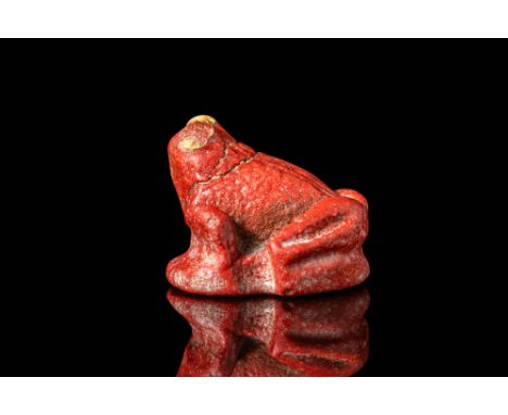 New Kingdom, Ca. 1550 - 1069 BC. A faience amulet in the form of a frog, glazed in deep red with contrasting yellow eyes. The
