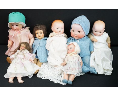 Seven Armand Marseille bisque headed dolls to include baby girl doll in pink overdress with green headpiece, with blue sleepi