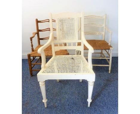 A white-painted open armchair with rattan-caned back and seat, together with two similar low ladder-back chairs (one painted 