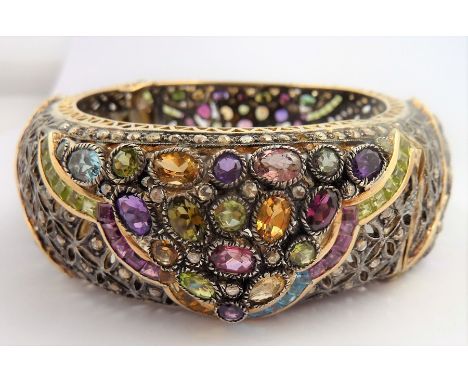 A large bangle profusely set with many diamonds and various other precious stones, marked 18K (total weight 102g)&nbsp;(The c