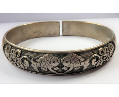 A boxed Chinese white-metal bangle decorated in relief with two opposing fish, the terminals with Chinese characters