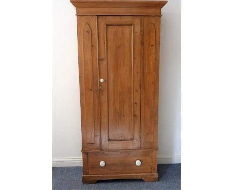 An early 20th century pine wardrobe of slim proportions; the outset cornice above a single panelled door and a full-width dra