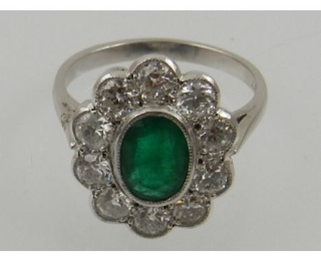 An 18 carat white gold, diamond, and emerald oval cluster ring. 