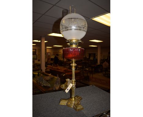 A Victorian brass table lamp with cranberry glass reservoir, clear and opaque shade, on triform base.