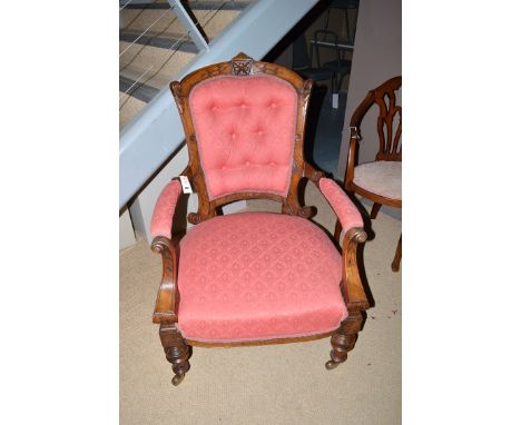 A Victorian carved walnut open arm easy chair, the button back, arms and seat upholstered in red floral material, raised on t