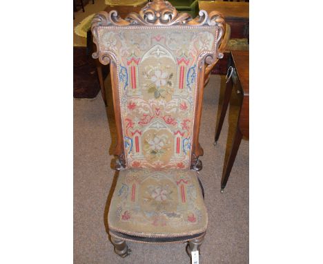 A Victorian walnut prie dieu chair, with woolwork tapestry back and seat, raised on turned legs terminating in brass castors.