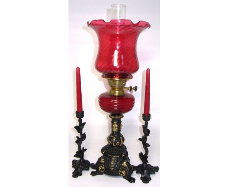 A black and gilt heightened Victorian oil lamp with cranberry shade, ruby glass reservoir and outstretched paw feet, height 6