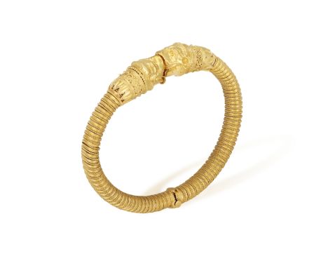 A 22K GOLD BANGLE  Of spring design, each terminal with opposing stylised Chimera heads, to a reeded bangle with scroll-wire 