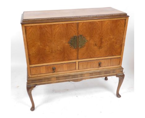 A mid century walnut drinks cabinet, with a pair of doors opening to reveal a single shelf, above two frieze drawers, raised 