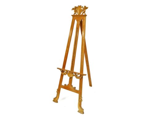 A Continental pine easel, the crest carved with two putti holding a vacant shield shaped cartouche, the support decorated wit