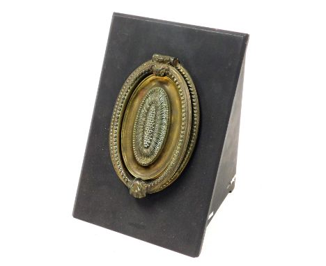 A Regency brass oval door knocker, with embossed leaf and beaded decoration, in a later wooden mount, 20cm high, 13cm wide.