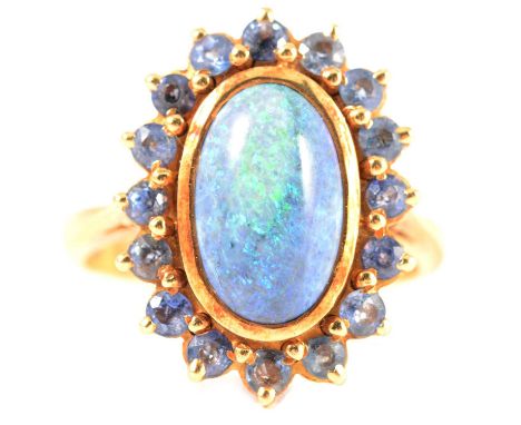 A black opal and sapphire dress ring, the oval cabochon cut opal 13mm x 8mm collet set and surrounded by sixteen claw set bri