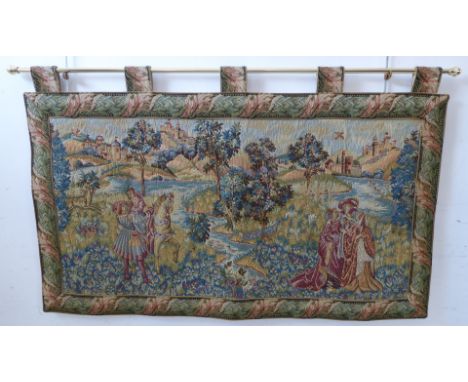 A wall-hanging cotton tapestry depicting a medieval style scene with buildings, castles, a lake, figures and a deer, on brass