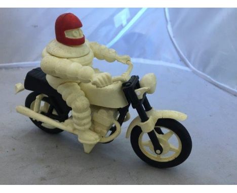 A Michelin Mr. Bibendum plastic figure riding a bicycle with a red helmet.