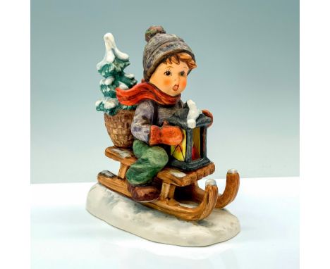 A figure of a young child in a blue jacket and hat with green pants sliding down a snowy hill on a sled. Goebel Hummel backst