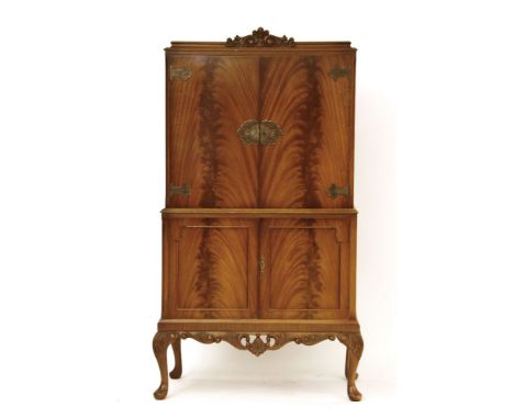 A mahogany cocktail cabinet, having a pair of panel doors enclosing mirrored interior above a further pair of panel doors on 